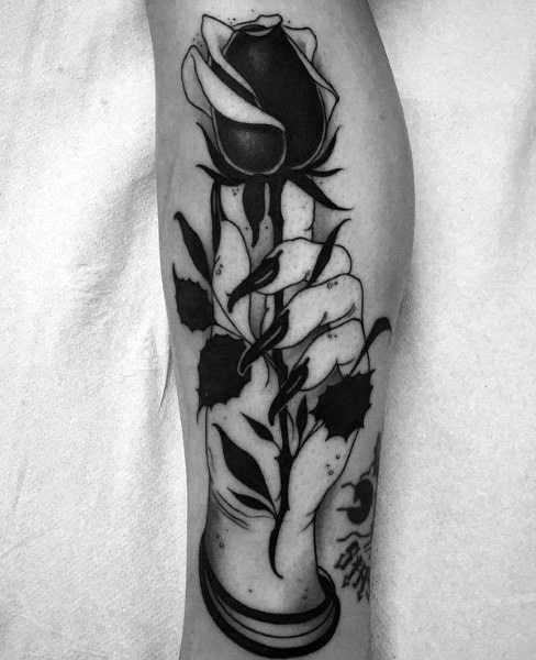 A black and white tattoo of a hand gently holding a rose, complete with its intricate stem, leaves, and thorns