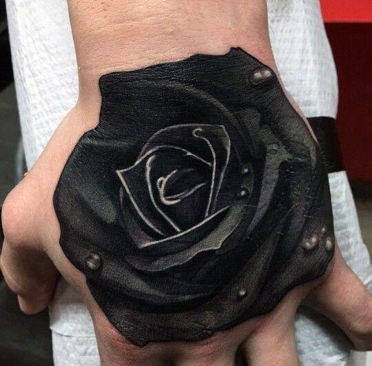 A realistic black rose tattoo on the back of a person's hand
