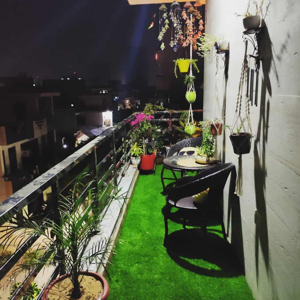 Nighttime balcony with artificial grass, potted plants, hanging planters, and a cozy seating area.
