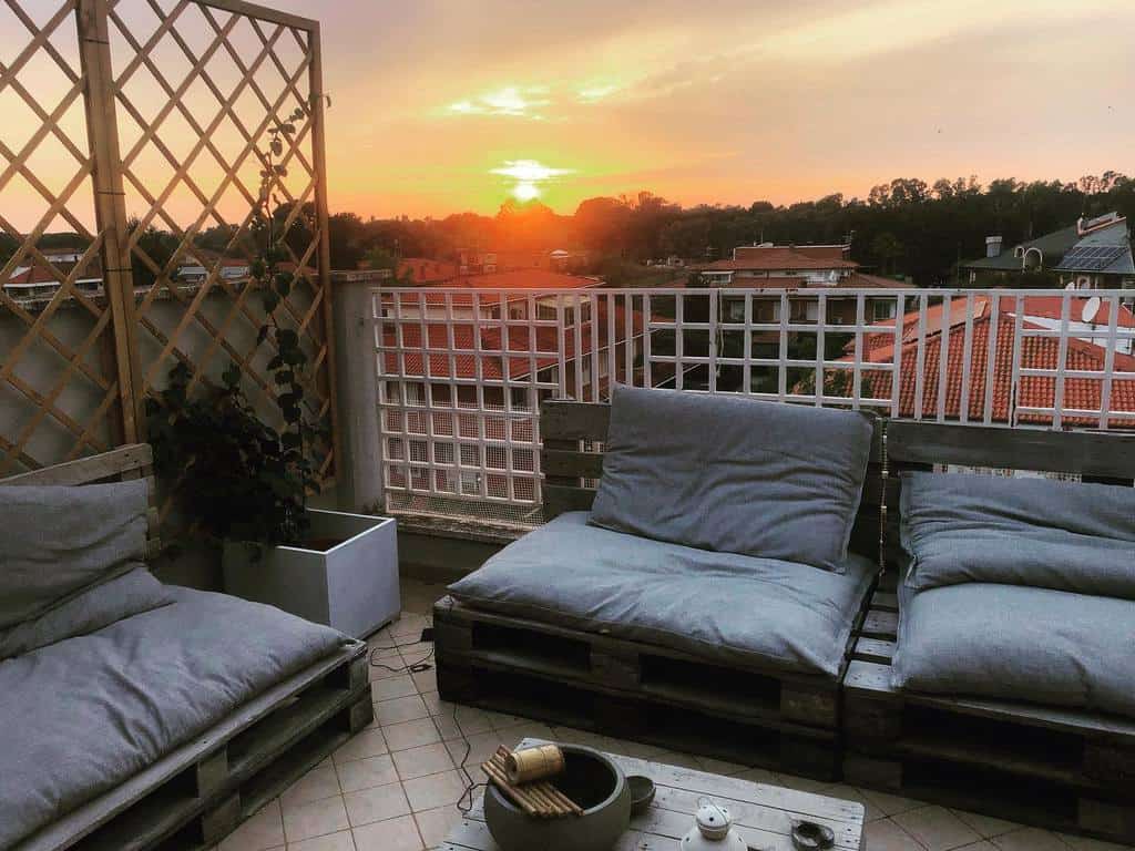 Sunset view from a cozy balcony with pallet seating, trellis, and soft cushions.