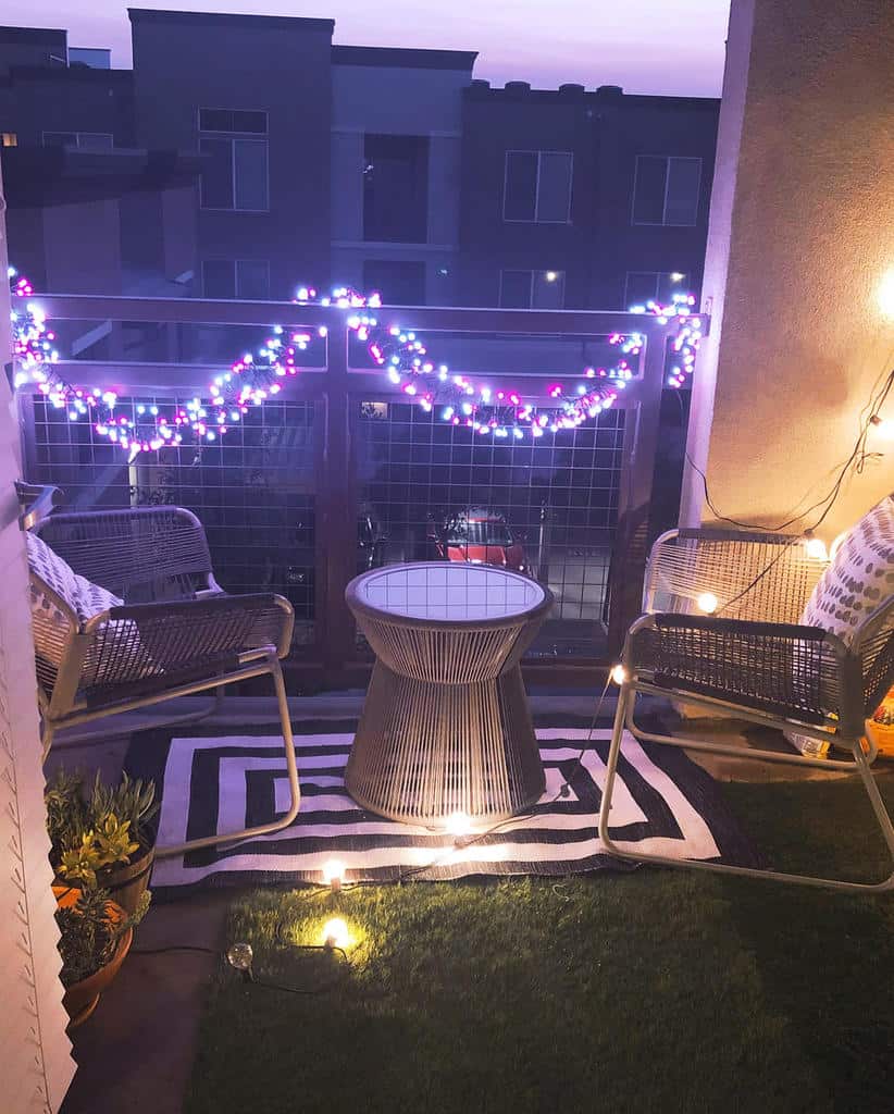 Cozy balcony at night with fairy lights, wicker chairs, small table, and artificial grass.