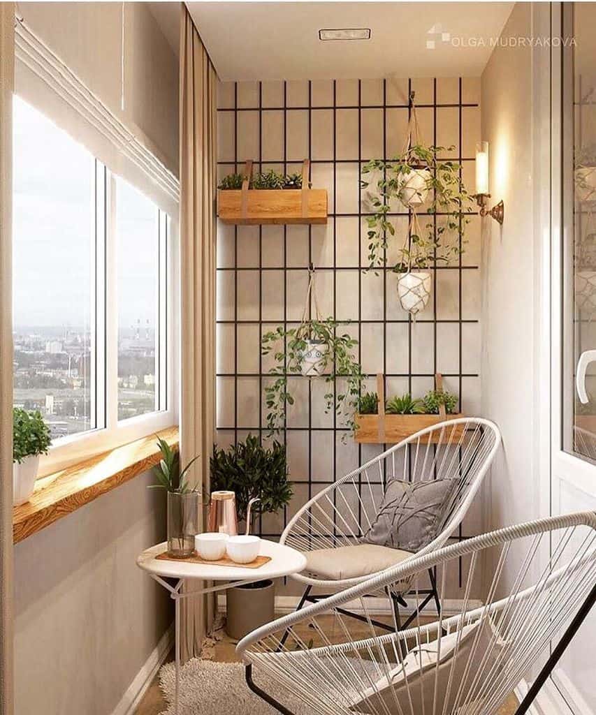 A cozy indoor balcony with a wire chair, plants on a grid wall, a small round table, and a panoramic window view
