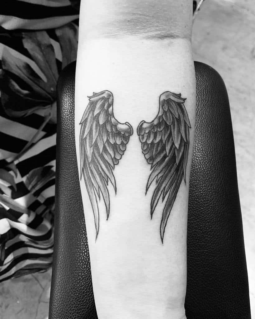 Black and white tattoo of angel wings with intricate shading that makes it realistic