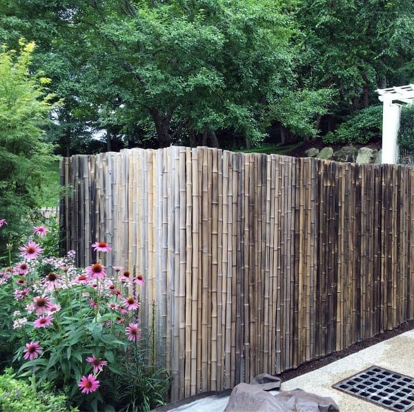 Natural bamboo fence creating a secluded backyard area, surrounded by lush greenery and flowers.