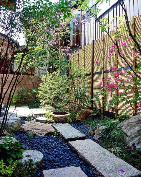 Horizontal bamboo fence in a serene garden featuring a stone pathway, vibrant flowering plants, and lush landscaping.