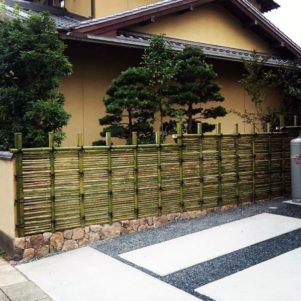 Horizontal bamboo fence with stone base next to a modern Japanese-style house exterior.