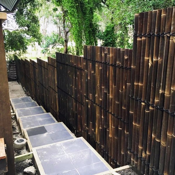 Dark bamboo fence along a narrow side yard walkway with stone steps and concrete borders.