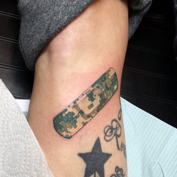 Realistic Band-Aid tattoo in digital camouflage pattern, placed on the ankle near star and script tattoos.