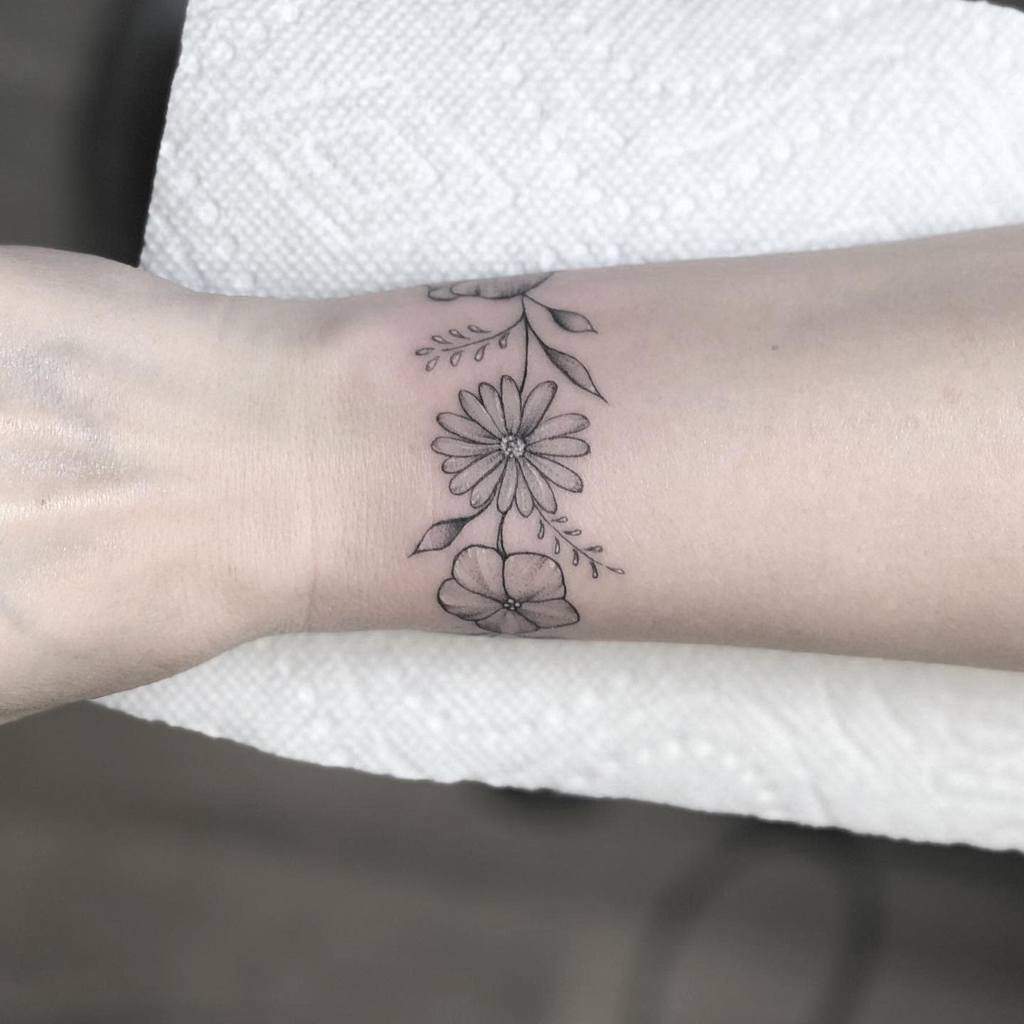 Delicate floral bracelet tattoo, featuring fine-line daisies and small violet flower blossoms intertwined with leaves for a subtle, elegant look