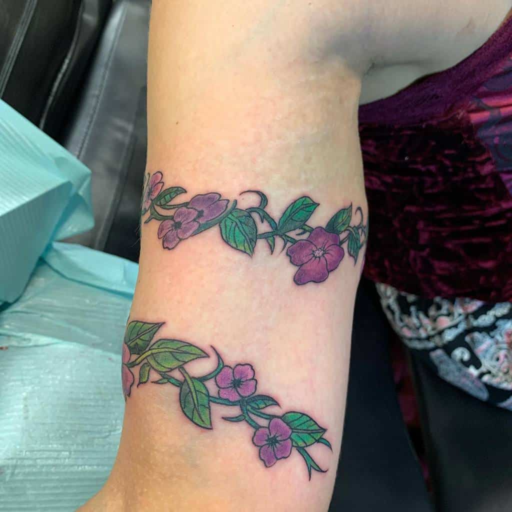 Vibrant floral armband tattoo featuring intertwined violet flowers and green leaves, creating a natural and elegant wrap-around design