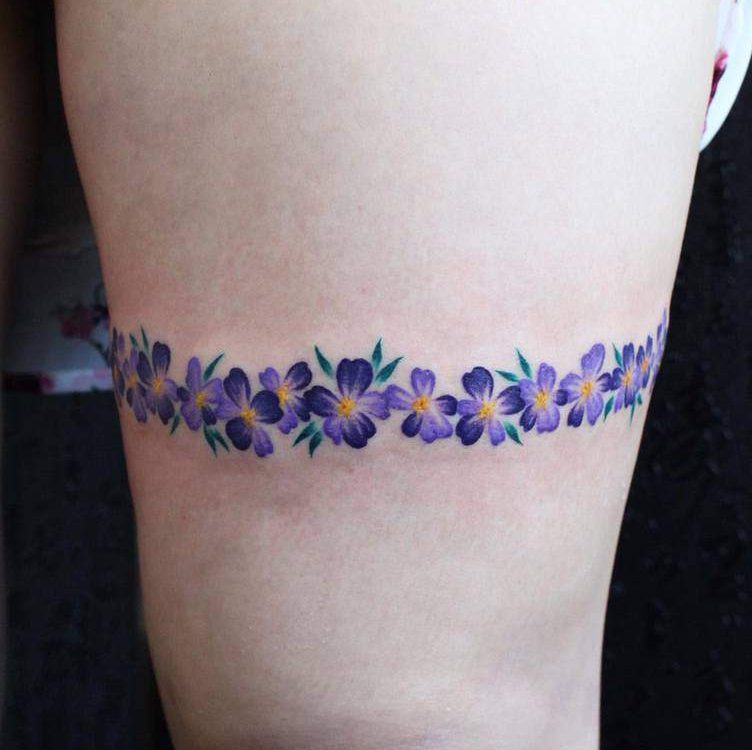 Delicate floral armband tattoo featuring a chain of vibrant purple violets with yellow centers and green leaves