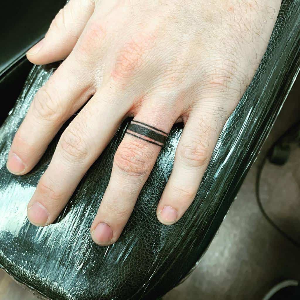 A minimalist tattoo of two black bands on a finger, symbolizing a wedding ring, with a simple and sleek design