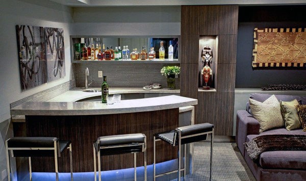 Modern bar with a variety of bottles, three stools, decorative art, and a cozy adjacent seating area