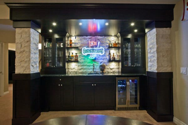 Home bar with dark wood cabinets, glass shelving, LED lighting, and a Heineken sign above the mini-fridge