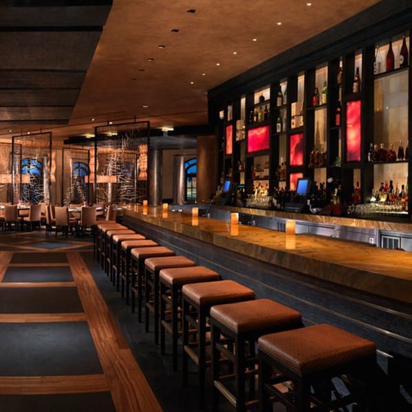 A sleek, modern bar with a long counter, high stools, and shelves of bottles softly lit in a warm ambiance