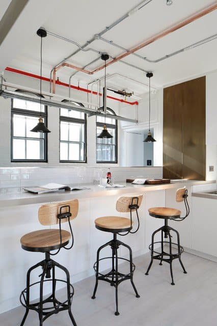 Industrial kitchen with metal bar stools, exposed pipes, and pendant lighting.
