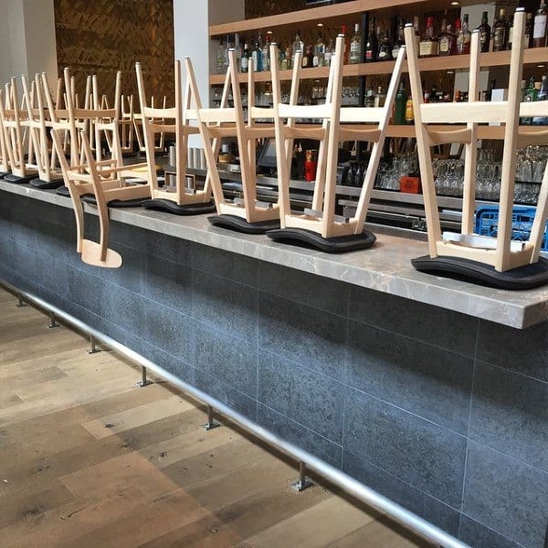 Wooden stools placed upside down on a bar top with a sleek, modern foot rail and a tiled bar front.