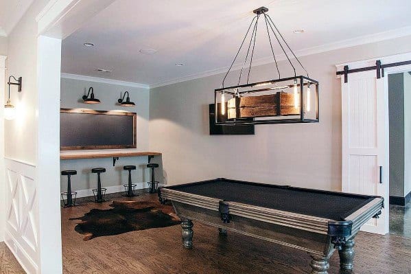Farmhouse-style billiard room with black pool table, rustic bar stools, and barn door accents.