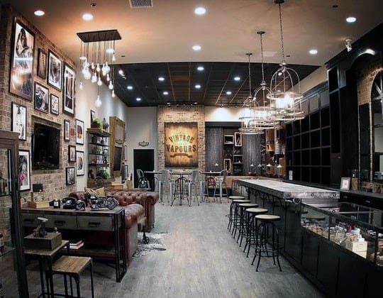 Vintage-themed café with brick walls, industrial lighting, leather sofa, bar counter with stools, and wall art display