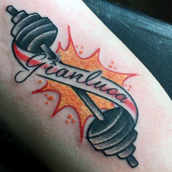 Barbell tattoo with bold weights and fiery background, featuring the name Gianluca in script, symbolizing strength and identity.