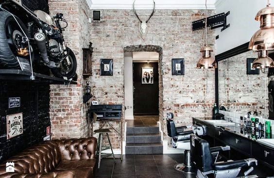 Industrial barbershop with exposed brick walls, leather sofa, and motorcycle decor.