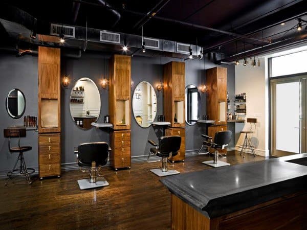 Modern barbershop with wooden cabinetry, oval mirrors, and sleek black chairs.