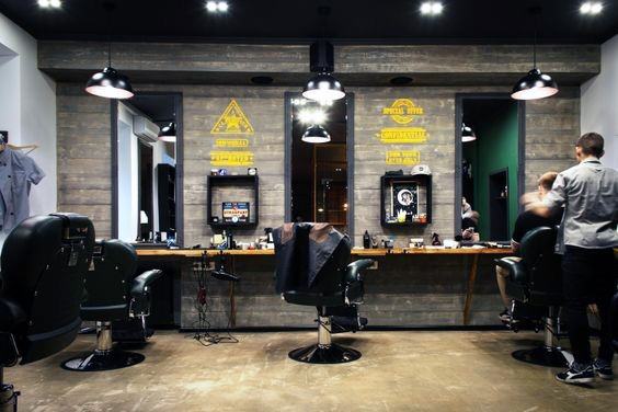 Modern industrial barbershop with black chairs, wood-paneled walls, and pendant lighting.