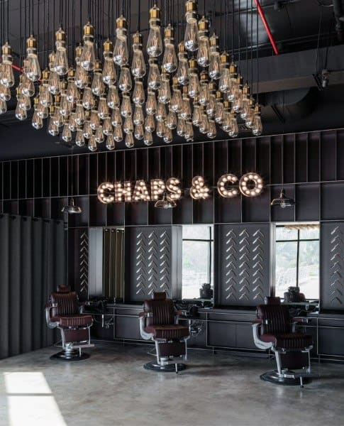 Modern barbershop with dark interiors, leather chairs, and a hanging bulb chandelier.