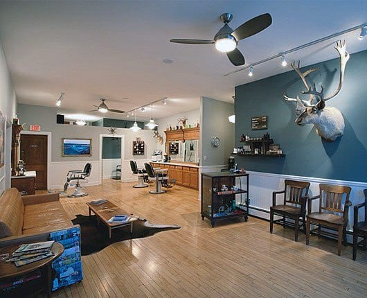 Spacious barbershop with wooden flooring, mounted antlers, and midcentury modern decor.