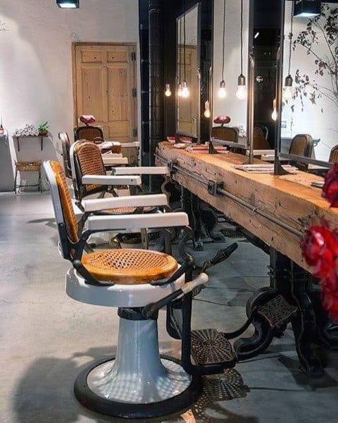 Rustic barbershop with vintage chairs, wooden table, and hanging pendant lights.