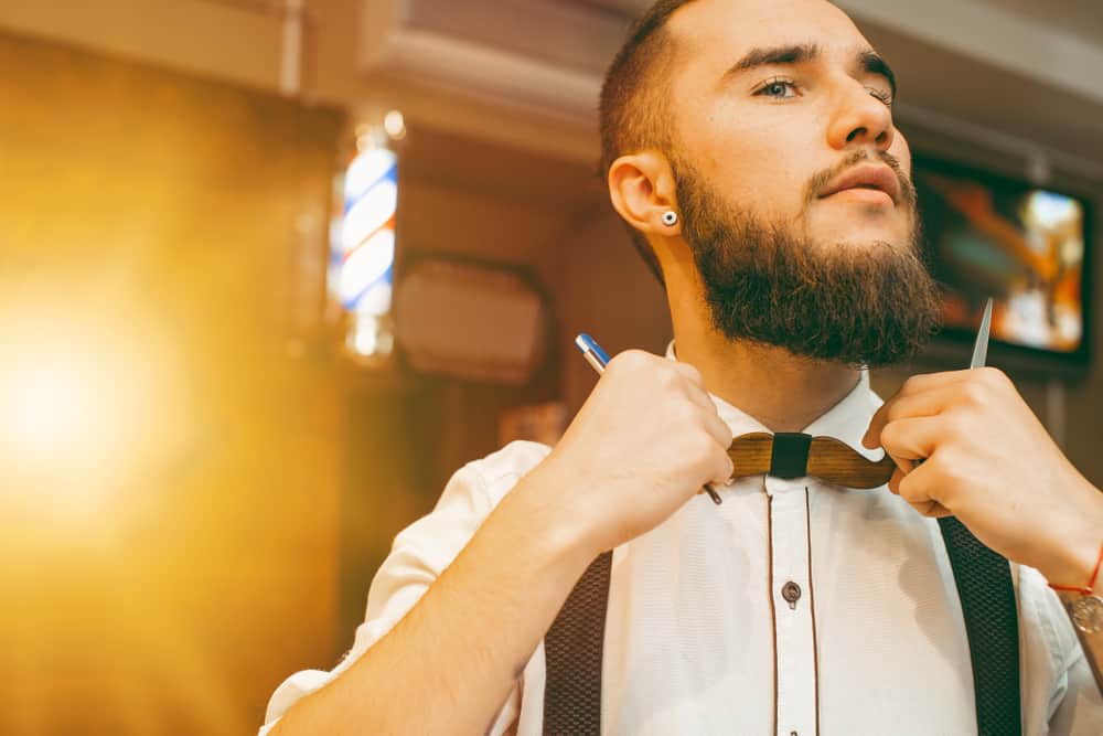 young handsome bearded barber straightens his bow tie