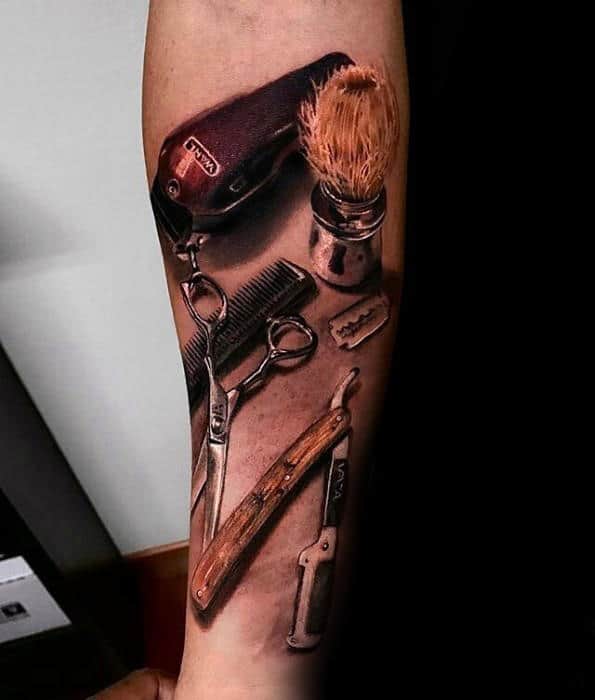 Tattoo of barber tools on an arm, including scissors, clippers, a brush, comb, razor blade, and straight razor with realistic detailing