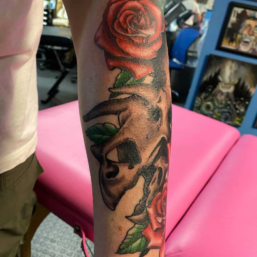 Tattoo of a detailed animal skull with vibrant red roses, blending realism and bold shading along the forearm.