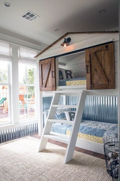 Children's bunk beds with a house frame and ladder featuring barn-style doors in a bright bunk room