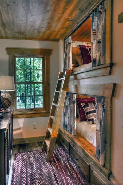 Cozy room with bunk beds, patterned curtains, and a ladder by a window offering a nature view on the left