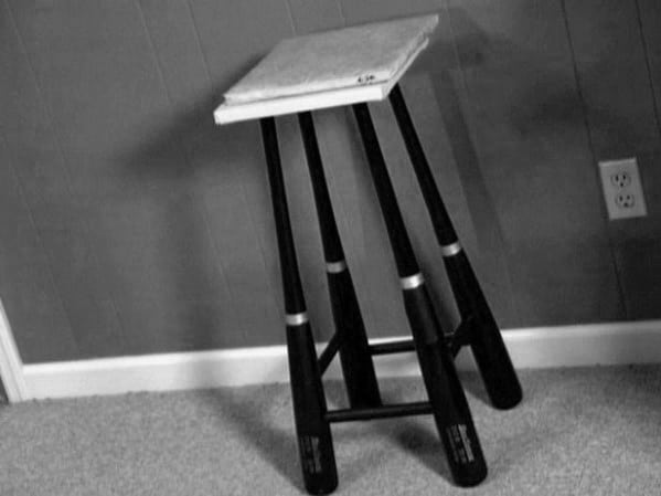 Side table made from stacked baseball bats and a flat top, against a wall with an electrical outlet