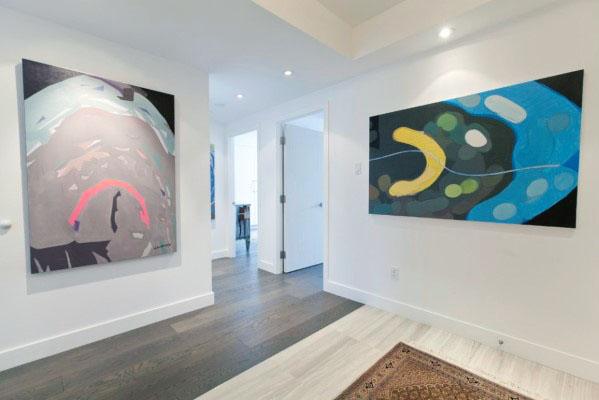Modern interior with white walls, colorful abstract art, and dark wood flooring.