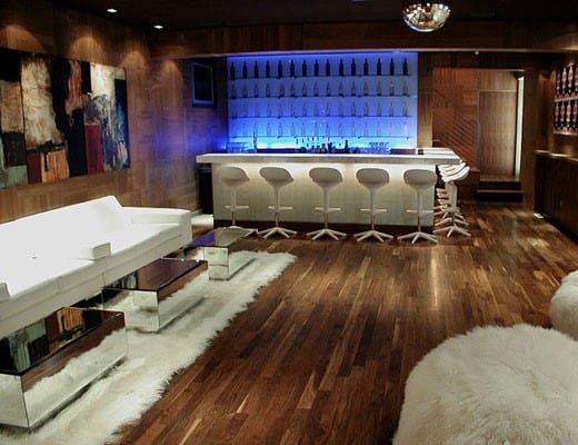 Chic modern lounge featuring a sleek white bar, swivel stools, plush sofas, abstract art, and wooden floors