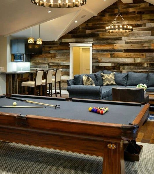 Basement with rustic wood walls, black pool table, sectional sofa, and chandelier-style lighting.