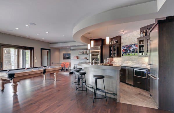 Stylish game room with a pool table, curved bar, stools, wall-mounted TV, and modern kitchen area
