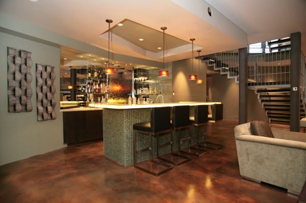 Modern bar with cushioned stools, pendant lights, and a stylish staircase in the background