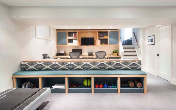 Built-in desk in a basement home office with chairs and shelving; foreground features a bench for gym equipment storage