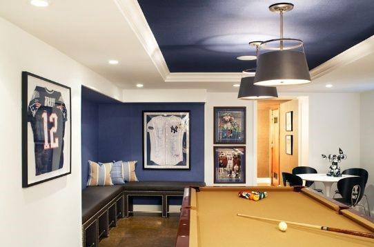 Sports-themed basement with pool table, framed jerseys, and sleek pendant lighting.