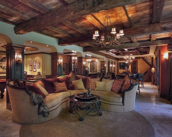 Luxurious basement with rustic exposed wooden beams, plush seating, and warm chandelier lighting.