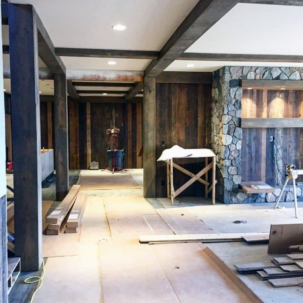Rustic basement under renovation with exposed wooden beams and stone accent wall.