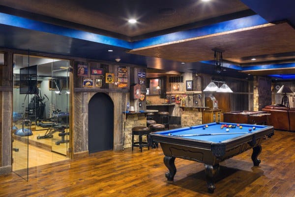 Basement with recessed cove ceiling, pool table, bar area, gym, and rustic wood flooring.