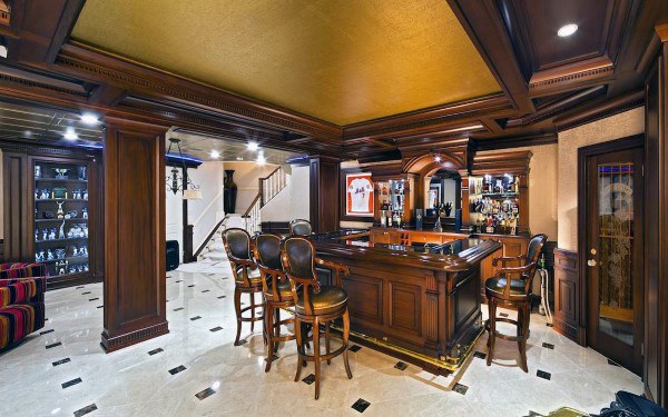 Luxurious basement bar with recessed cove ceiling, wood paneling, and marble flooring.