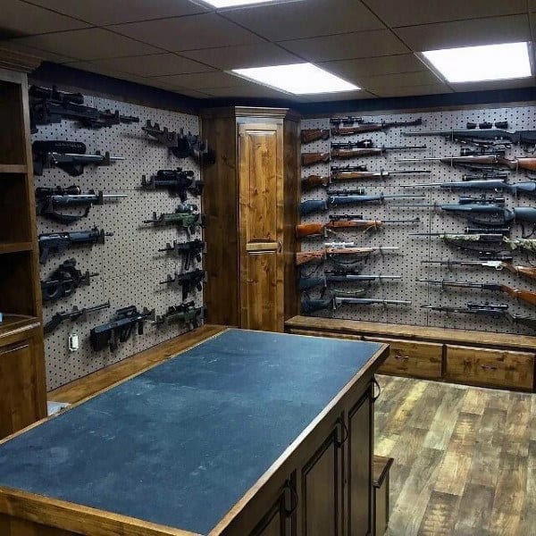 Basement gun room with pegboard walls, wooden cabinets, and a central work table.