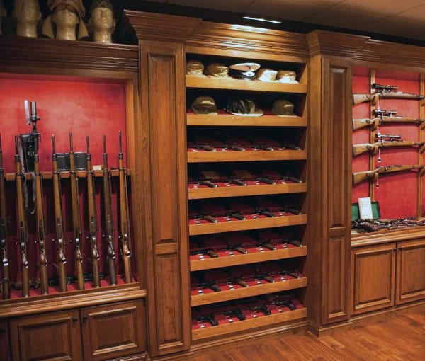 Gun room with wooden shelves displaying rifles, pistols, and collectible military helmets.