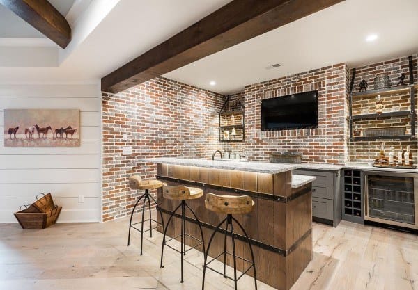 Rustic basement bar with exposed brick walls, wooden stools, and recessed lighting.